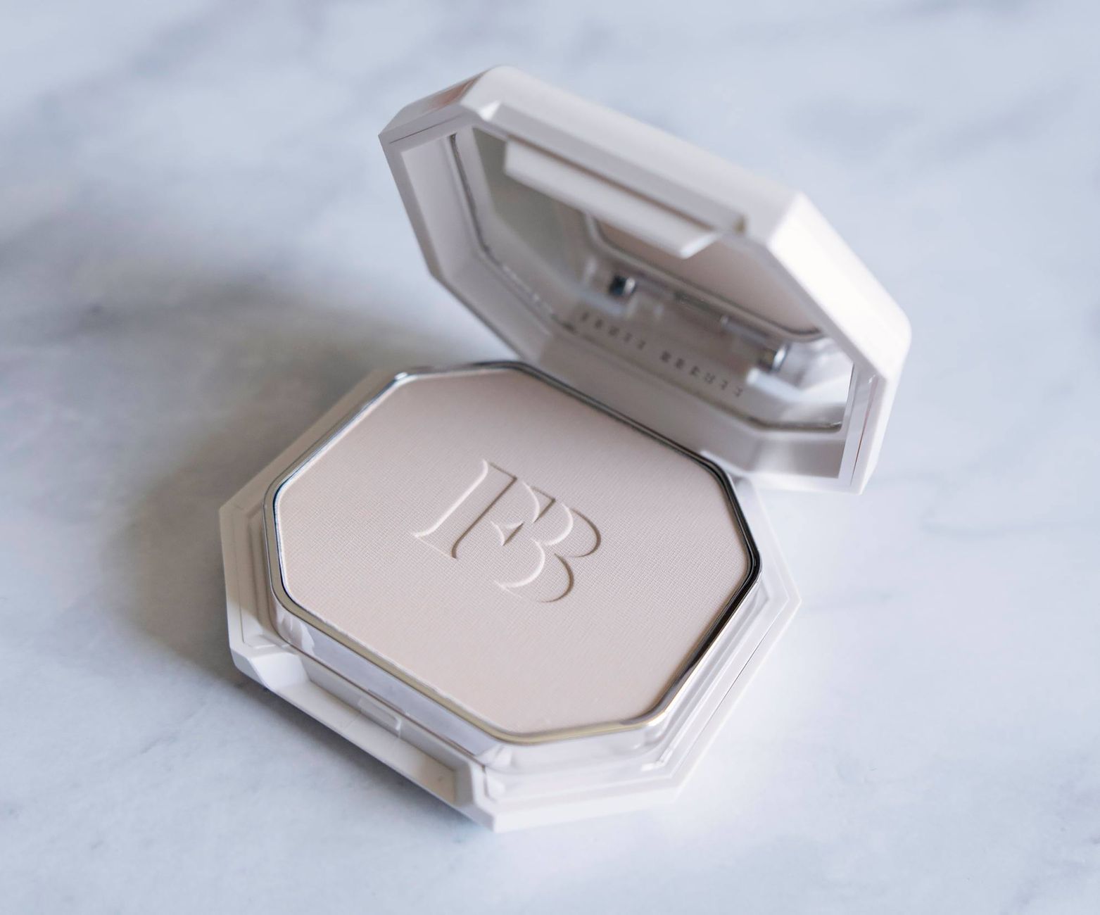 Close-up of an open compact powder with embossed logo on marble background.