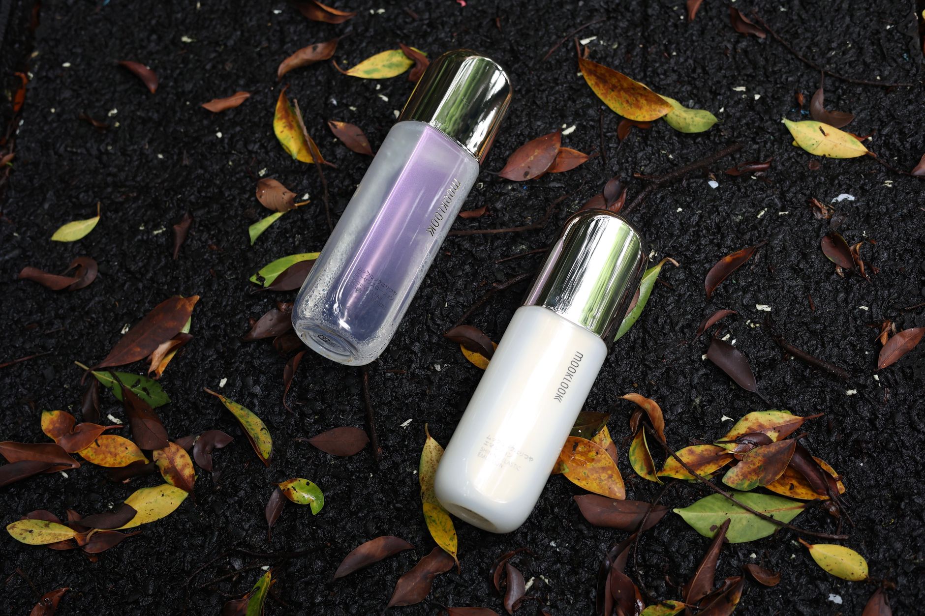 Two elegant skincare bottles on a dark, leaf-strewn surface, showcasing beauty and elegance.
