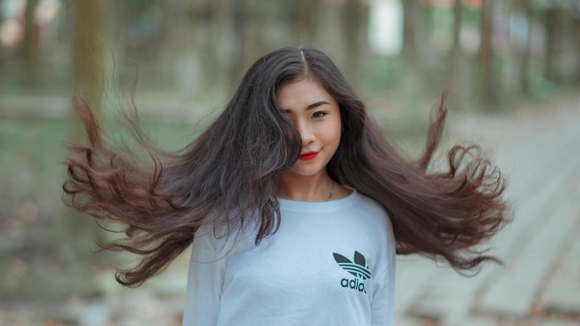Young woman outdoors with flowing hair and playful pose in a white shirt.